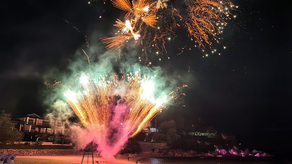Vibrant fireworks explode in a colorful display over a beach at night, illuminating the sky with bright hues and smoke.