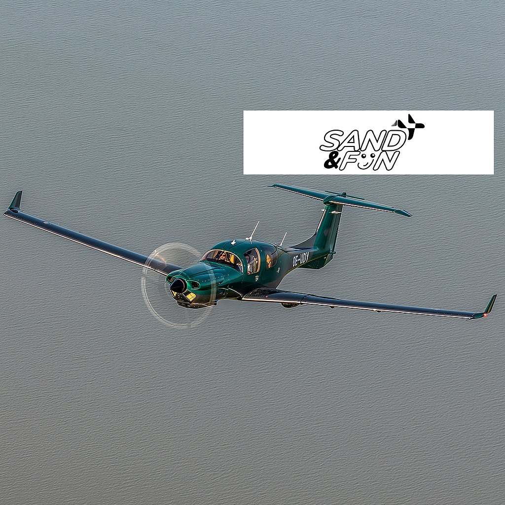 A sleek green aircraft soars gracefully above a calm body of water, showcasing its elegant design and spinning propeller.