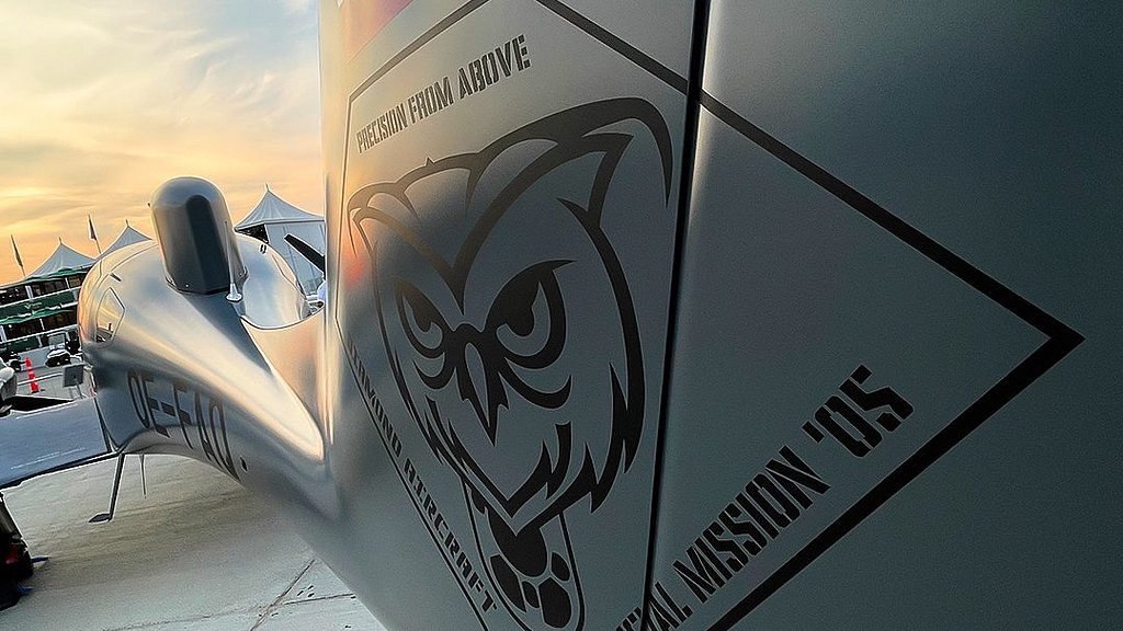 A close-up view of a special mission aircraft's side, featuring an owl emblem and the phrase 'Precision from Above' against a sunset backdrop.