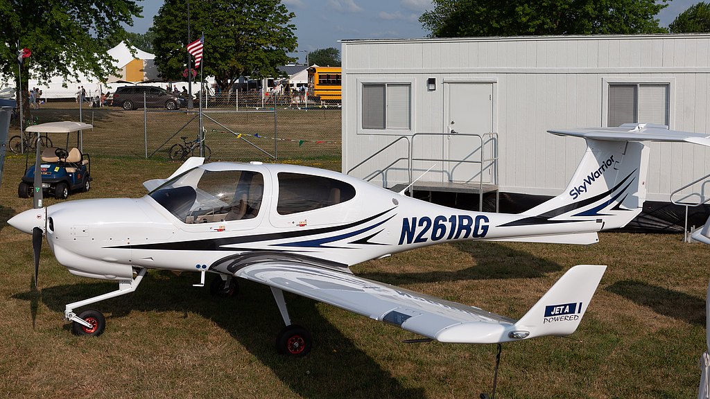 A sleek white aircraft with blue accents is parked on grass, showcasing its propeller and registration number N261RG.