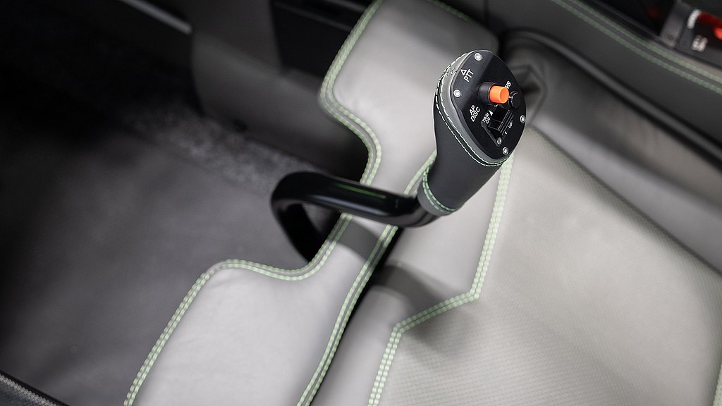 A close-up view of a sleek leather pilot stick, featuring a black handle with control buttons and a vibrant orange switch.