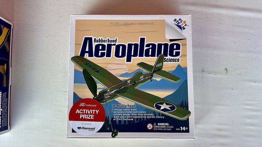 A vintage rubber band aeroplane model box featuring a P-40 Warhawk design, showcasing a scenic mountain backdrop.