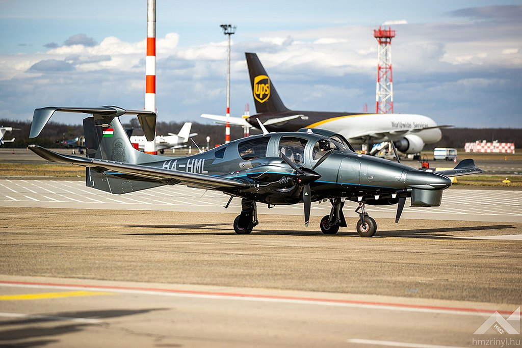 DA62 MPP standing on the airport in front of larger aircraft. 