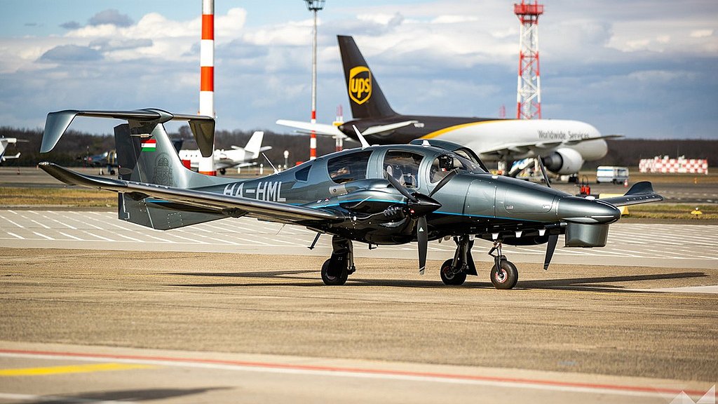 DA62 MPP standing on the airport in front of larger aircraft. 