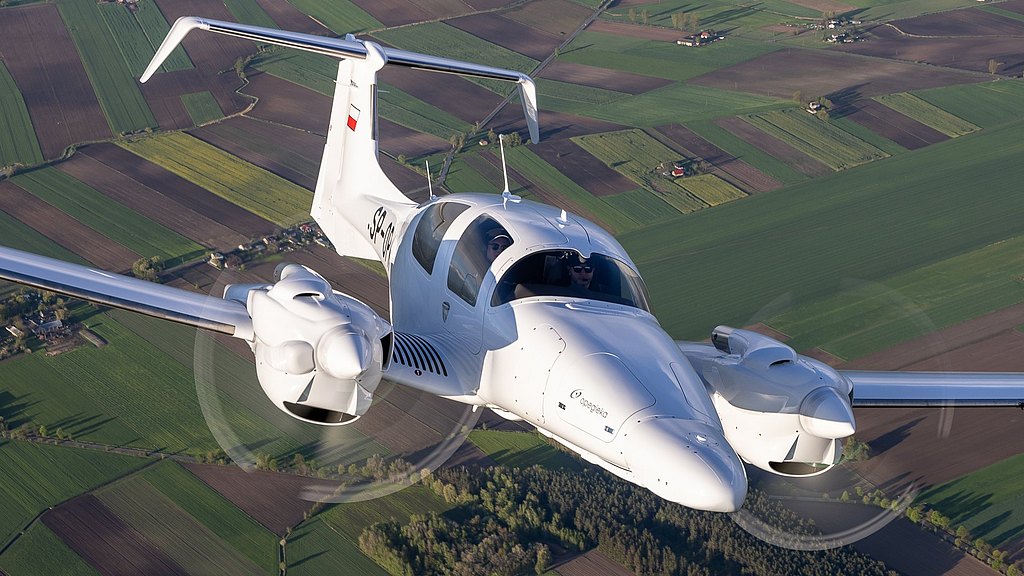 In mid-flight, a DA62 MPP twin-engine plane navigates through the air, revealing a stunning view of cultivated fields below.