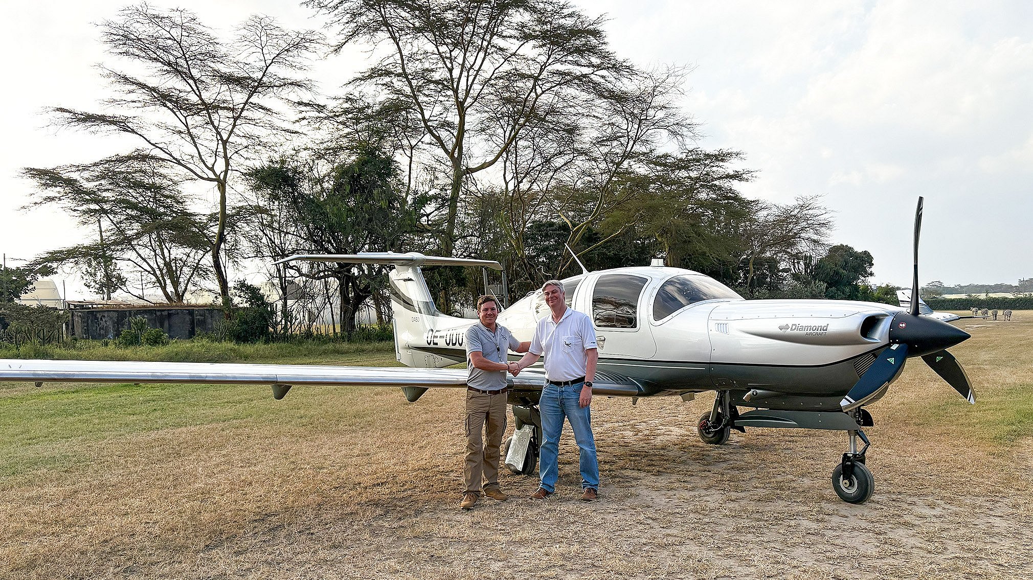 Zwei Männer schütteln sich vor einem Diamond DA50 Flugzeug die Hand auf einem Flugfeld in Afrika.
