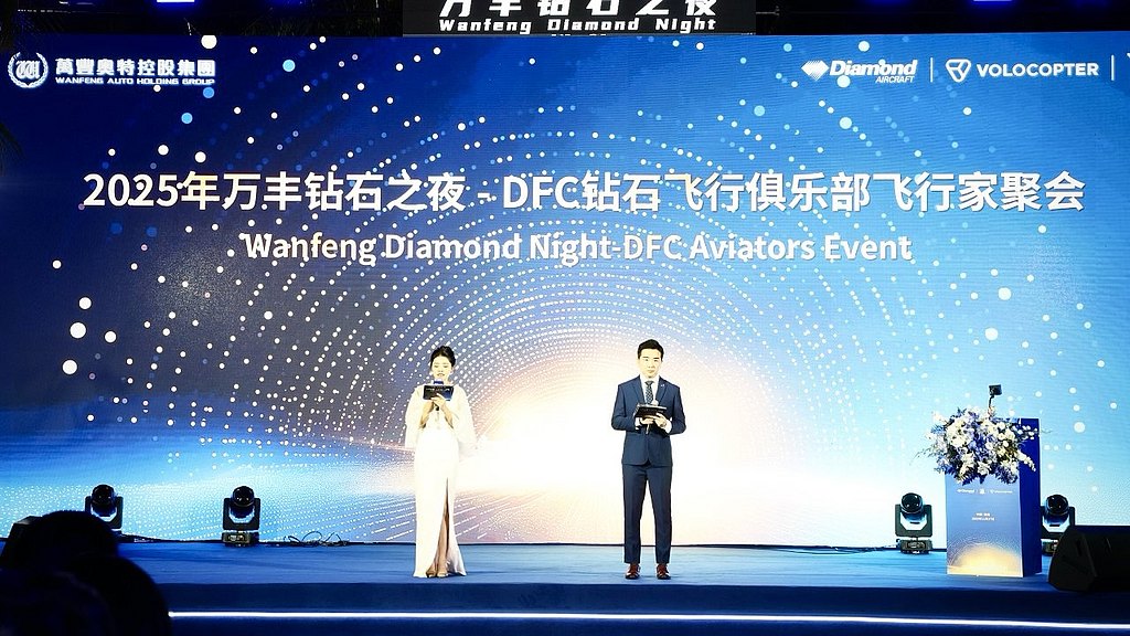 A woman in a white dress and a man in a suit stand on stage, presenting at the Wanfeng Diamond Night event.