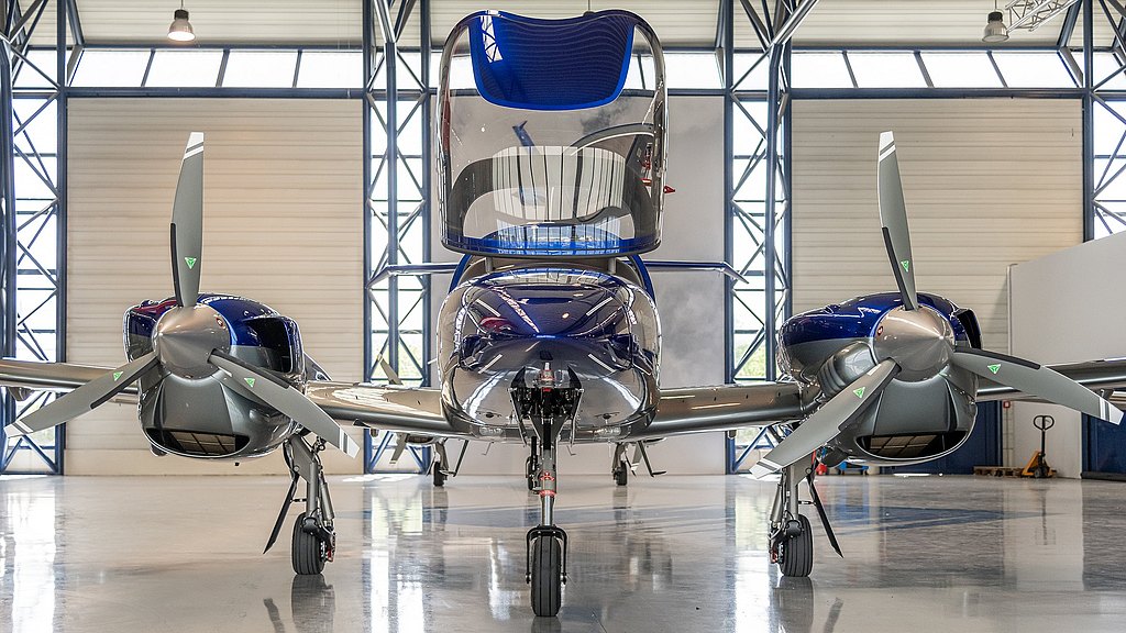 Blue DA42-VI with open canopy standing in a hangar.