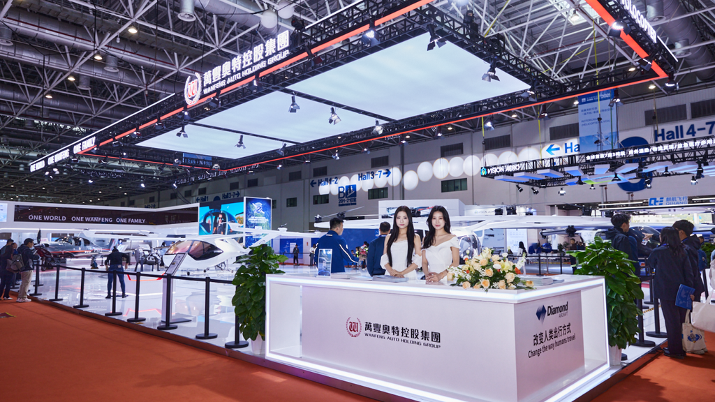 The scene captures a lively aviation show with two women beside a stylish counter, surrounded a DA50 RG and a Volocity-