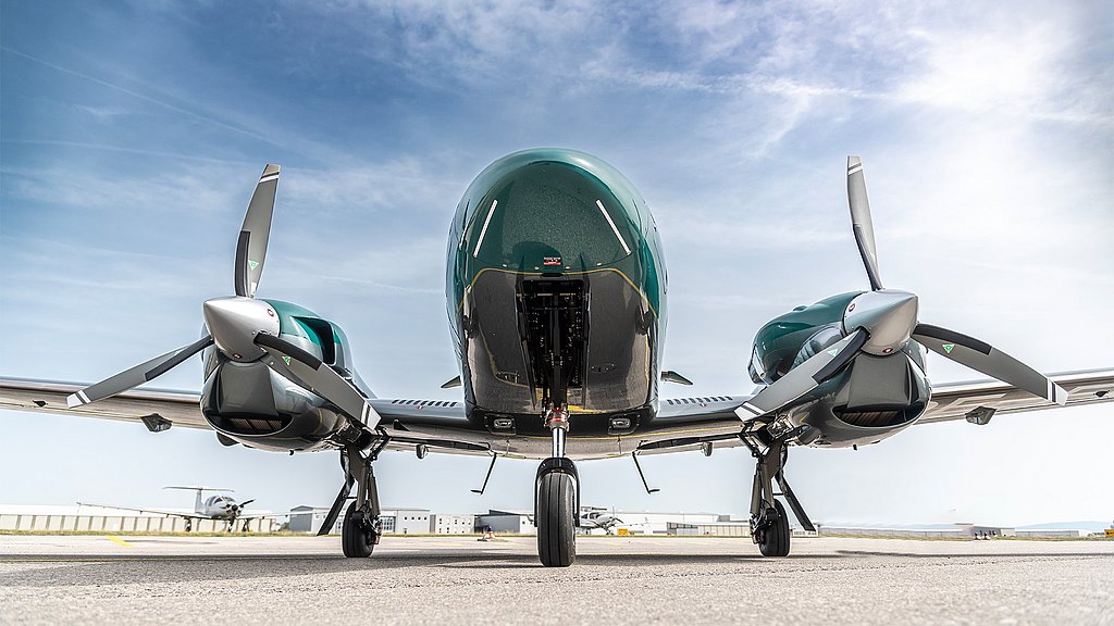 A sleek aircraft stands on the tarmac, showcasing its twin engine and propellers against a clear blue sky.