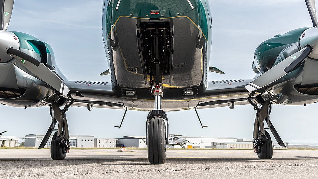 A sleek aircraft stands on the tarmac, showcasing its twin engine and propellers against a clear blue sky.