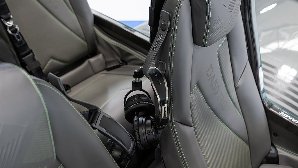 A sleek, modern aircraft seat features a headset holder, showcasing a stylish design with green stitching and ergonomic support.