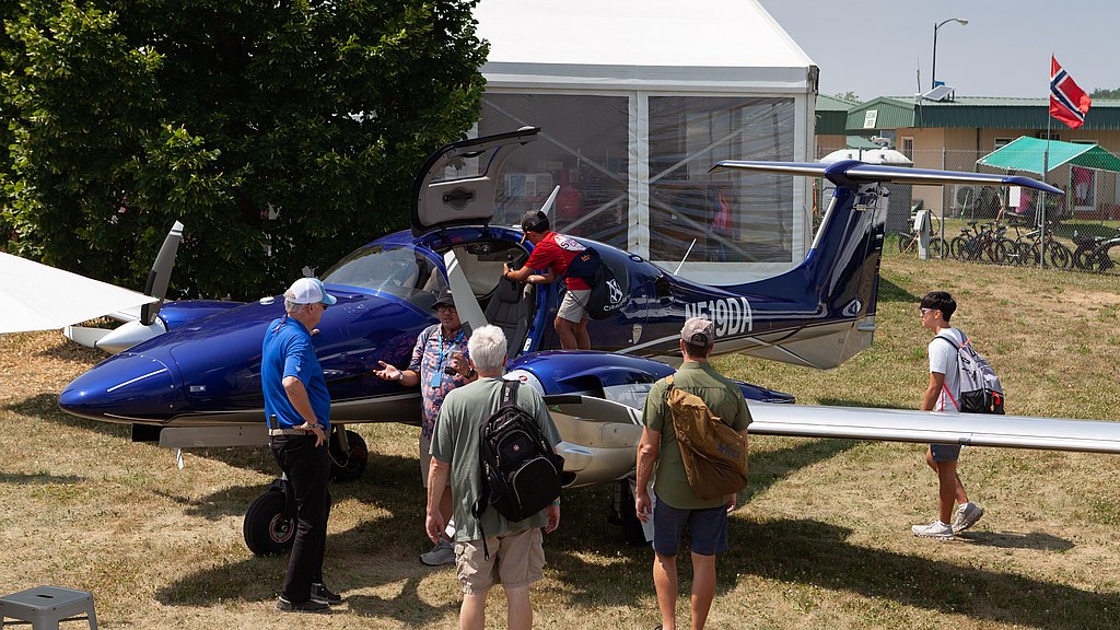 A group of people gathers around a blue aircraft, with one person climbing inside while others engage in conversation.
