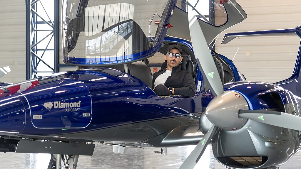 Man sitting in a blue DA42-VI parked in a hangar.