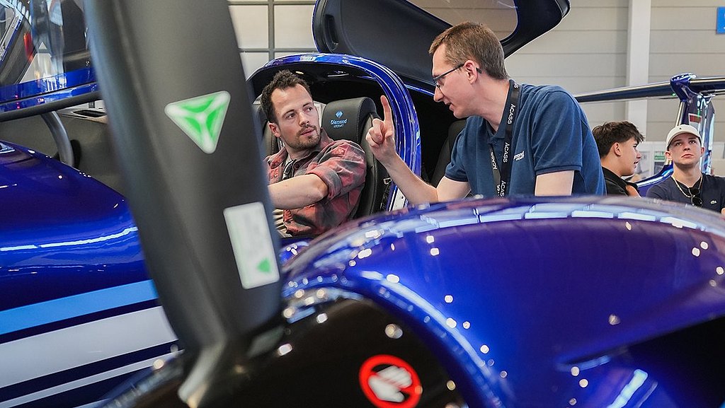 Two men engage in a lively discussion inside a blue DA42-VI aircraft, showcasing a modern aviation design.