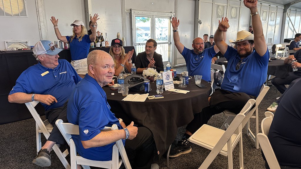 A lively group of people in blue shirts celebrate together, raising their hands in excitement at a social event.