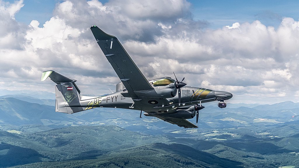 DA62 MPP Guardian flying over green hills.