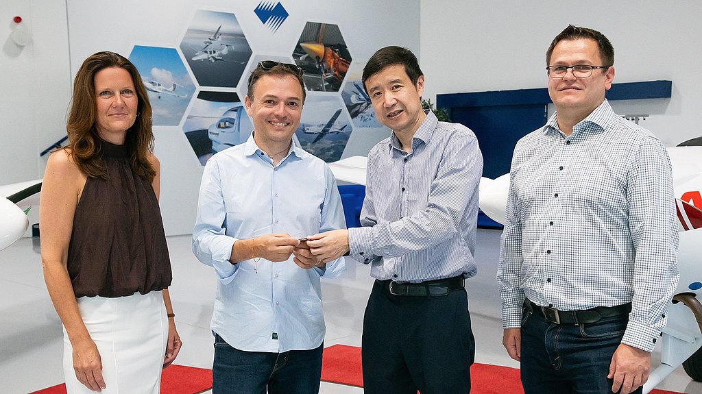 A group of four professionals stands together in a modern aviation facility, smiling and engaging in a handshake.