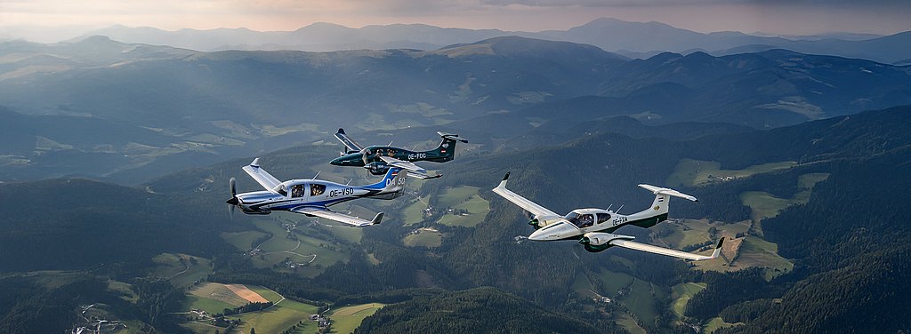 Three Diamond aircraft soar gracefully through the sky, surrounded by lush green hills and distant mountains under a soft sunset glow.