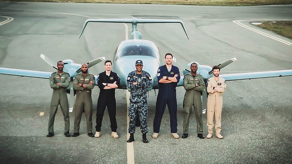 A diverse group of six pilots stands confidently in front of a DA62 MPP  aircraft on a runway, showcasing camaraderie and professionalism.