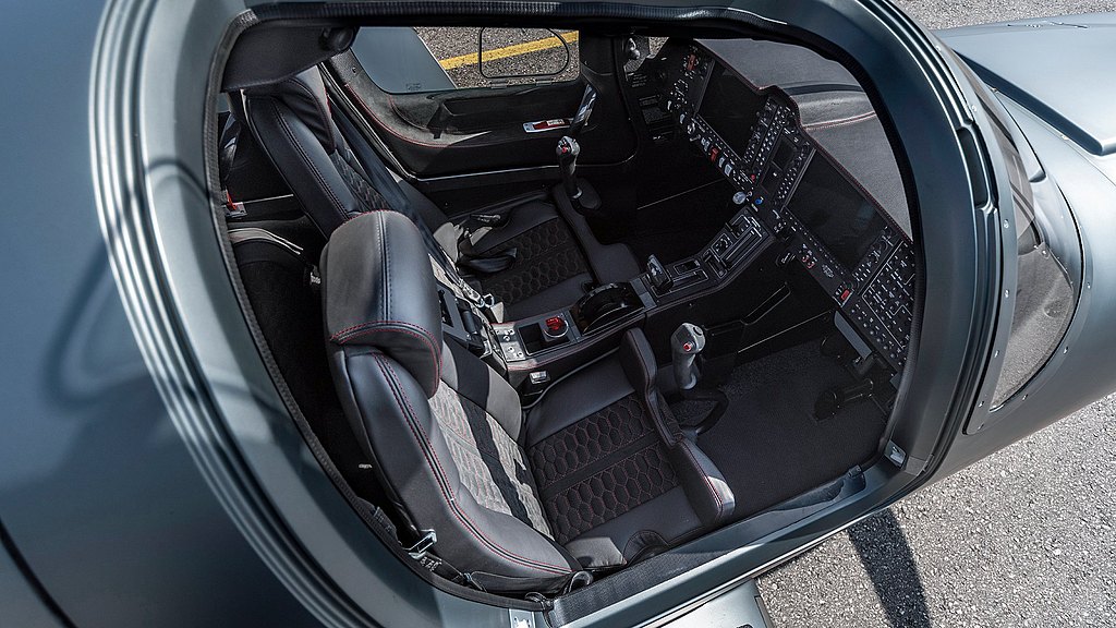 The interior of a sleek DA50 RG aircraft showcases modern black leather seats with red stitching and a high-tech control panel.