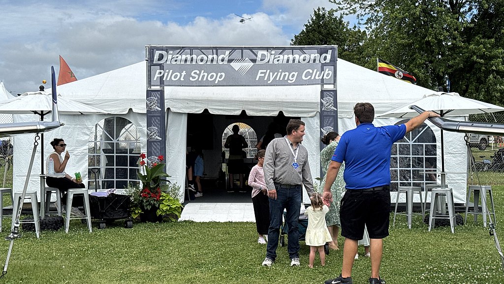 Visitors gather at the Diamond Pilot Shop, where a man gestures towards the entrance while a child holds his hand.