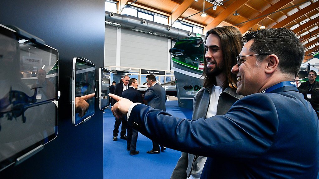 Two men engage enthusiastically with interactive displays at an aviation exhibition, showcasing their interest in the 3D configurator.