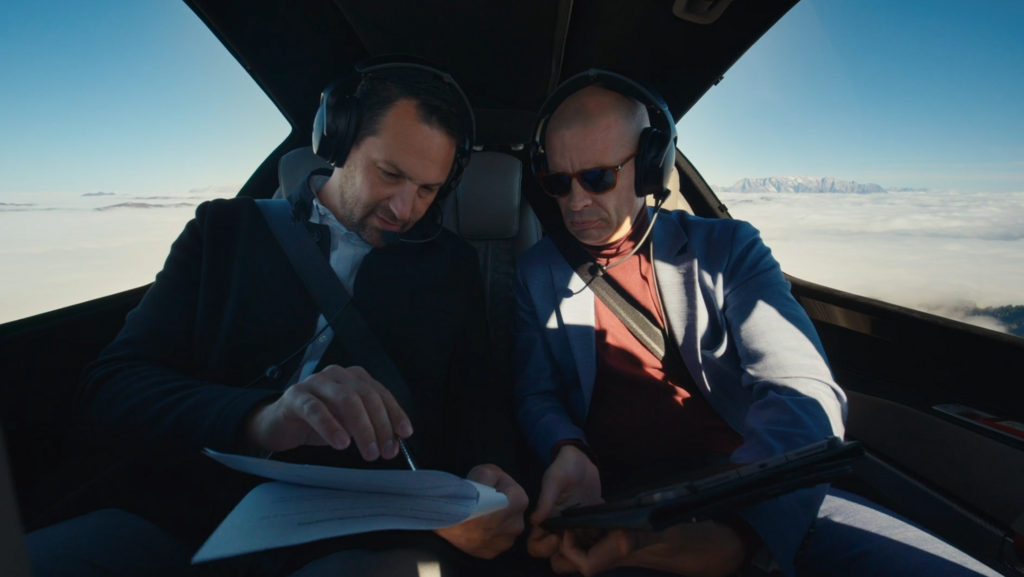 Two men in a in a DA62 review documents, surrounded by clouds and mountains, showcasing a serene business aviation experience.