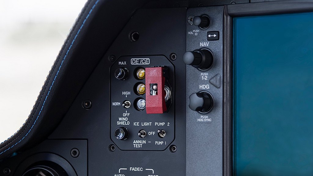 The interior of an aircraft cockpit, showcasing a mix of buttons and knobs, including a prominent red switch for TKS deicing system..