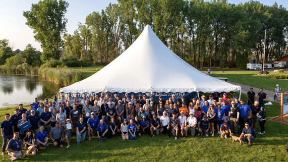 Large group of people standing in front of a tent at a lake.