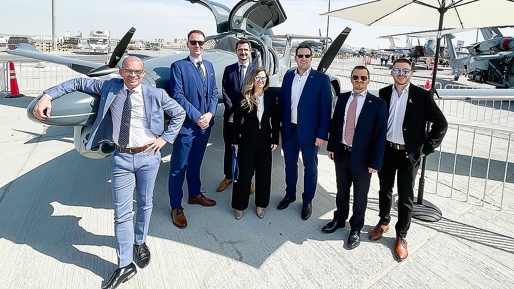 A diverse team of seven stands proudly next to a cutting-edge aircraft, reflecting a dynamic atmosphere of business and aviation excellence.