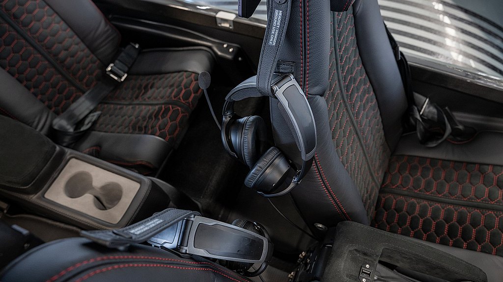 A close-up view of a sleek aircraft interior featuring black leather seats with red stitching and a headset mounted on the side.