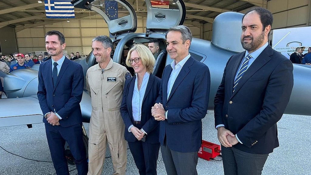 A group of five individuals stands in front of a sleek aircraft, smiling and dressed in formal attire.