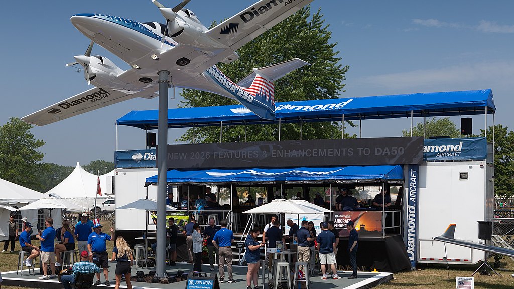 A large model airplane hangs above a busy booth, where attendees engage with staff and explore aircraft features.