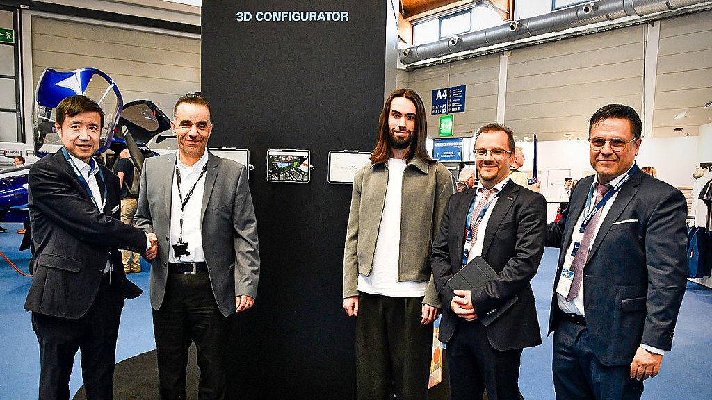 A group of four men stand together, smiling, in front of a display labeled '3D CONFIGURATOR' at an event.