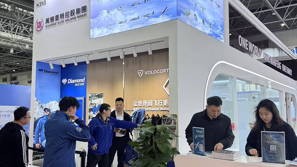 A busy exhibition booth featuring the Diamond Flying Club, showcasing various aircraft images on a large screen above.