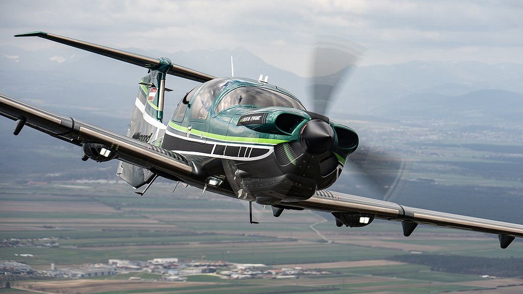 This image features a stylish DA50 RG aircraft in flight, highlighting its unique color scheme and the expansive landscape beneath it.