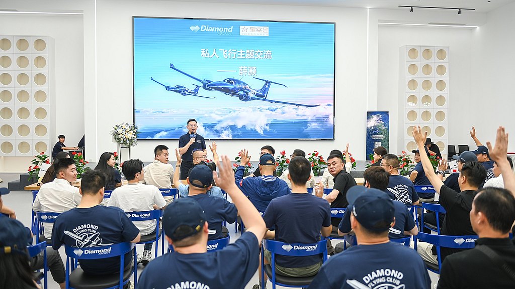 A speaker engages an audience in a modern conference room, with attendees raising hands to ask questions about aviation.