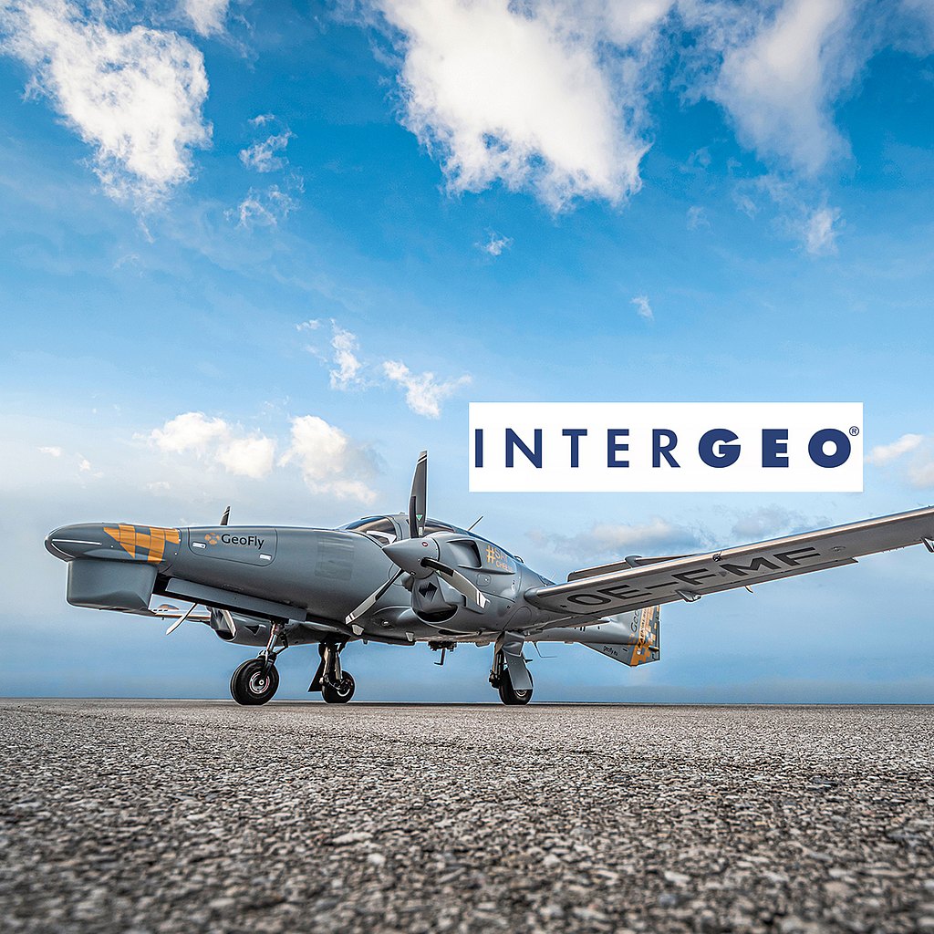 A gray DA62 MPP aircraft is parked on a runway, with a bright blue sky and fluffy clouds in the background.