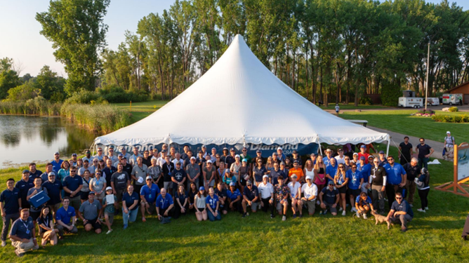 Large group of people in front of a tent at a lake.