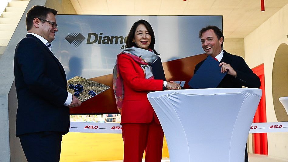 A celebratory moment unfolds as a woman in red and a man in black shake hands, while another man presents a decorative gift.