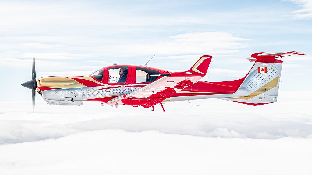 The vibrant DA50 RG aircraft, adorned with a Canadian flag, glides gracefully through a bright sky, surrounded by fluffy white clouds.