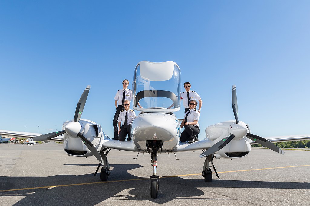 A group of four aviation students stands proudly on a DA42 aircraft, embodying excitement and ambition in their flight training.