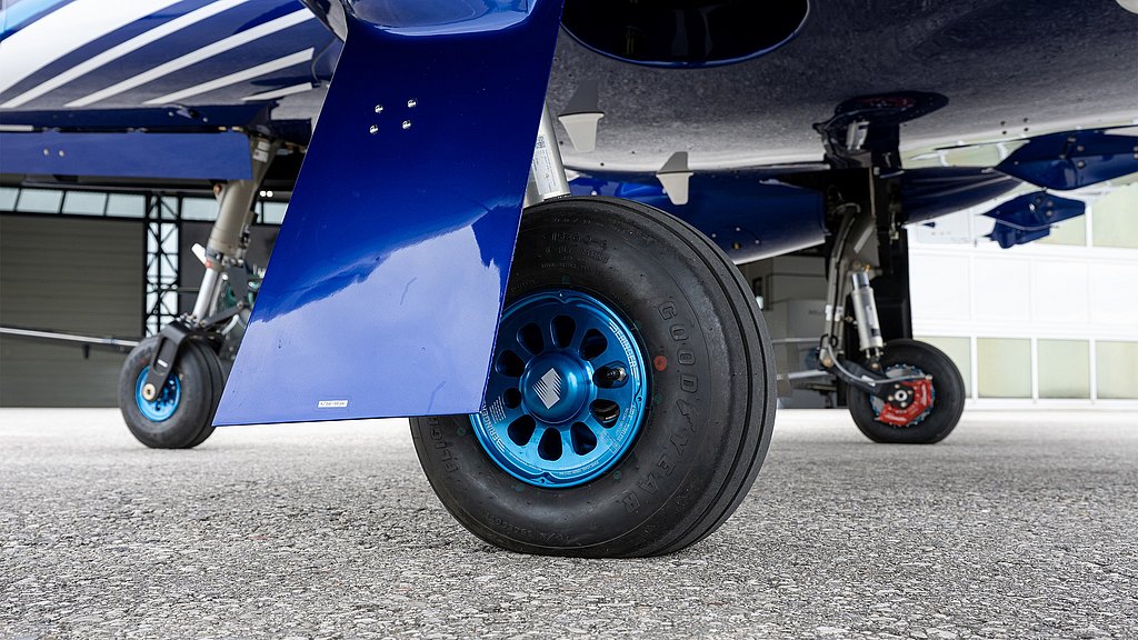 The image captures a detailed view of an aircraft wheel, featuring a blue hub and showcasing the surrounding aircraft structure.