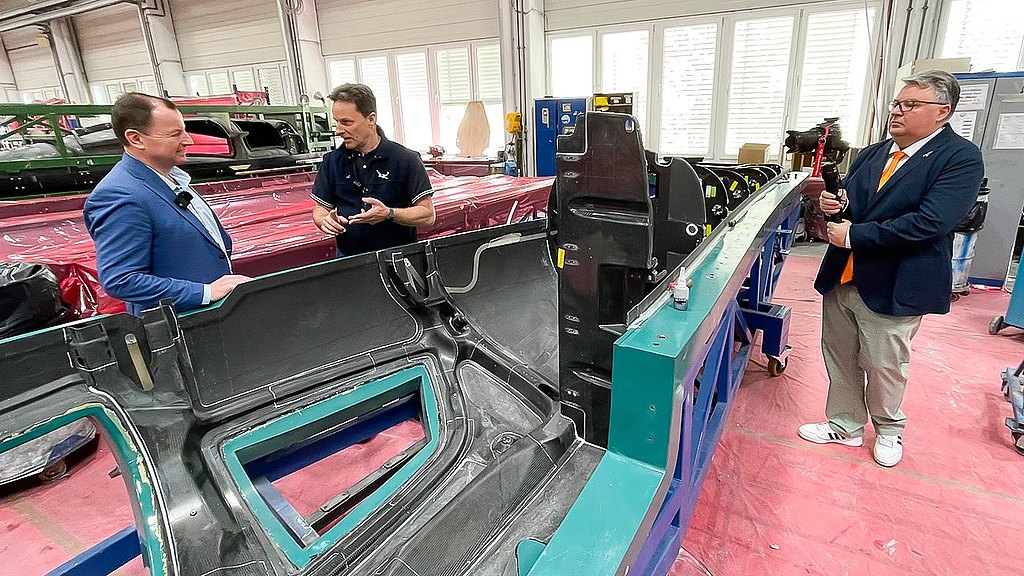 Two men engage in conversation while examining a large, partially assembled component in a manufacturing facility.