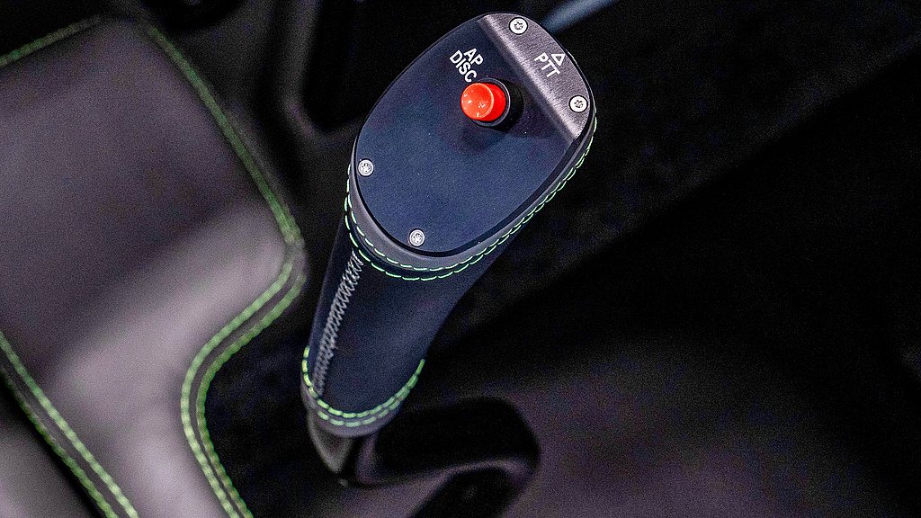 A close-up of a pilot's control stick featuring a red button and sleek black leather with stitching.