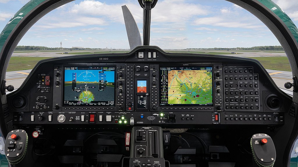 Inside the aircraft cockpit, two large digital displays show flight metrics and navigation maps, while controls are neatly arranged.