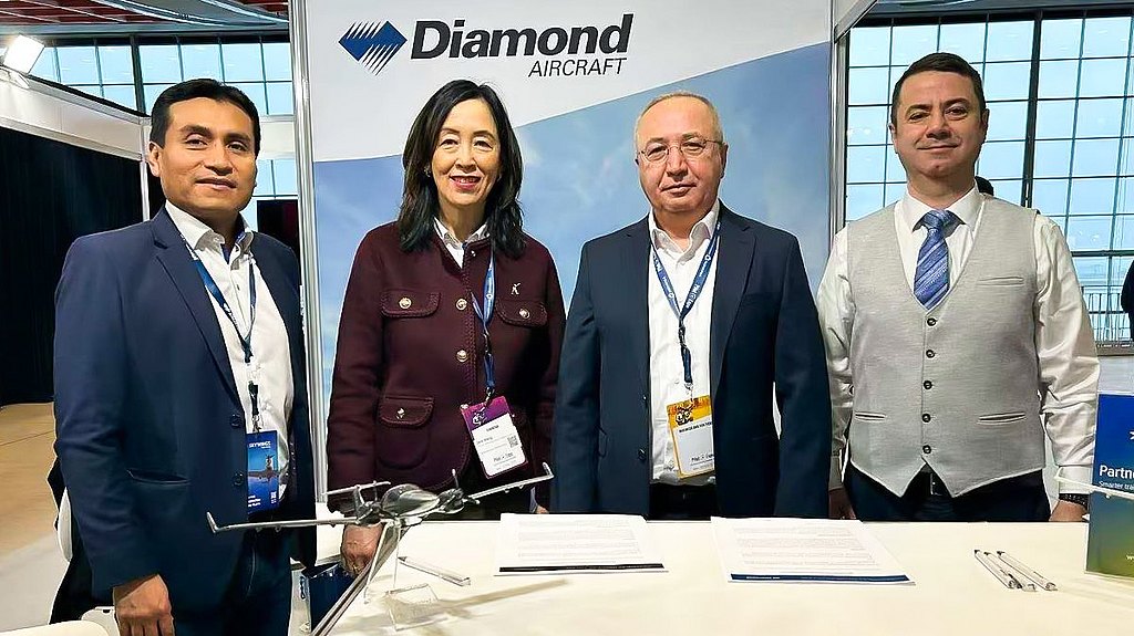 Four professionals stand together at a trade show booth, showcasing a model aircraft and engaging in conversation.