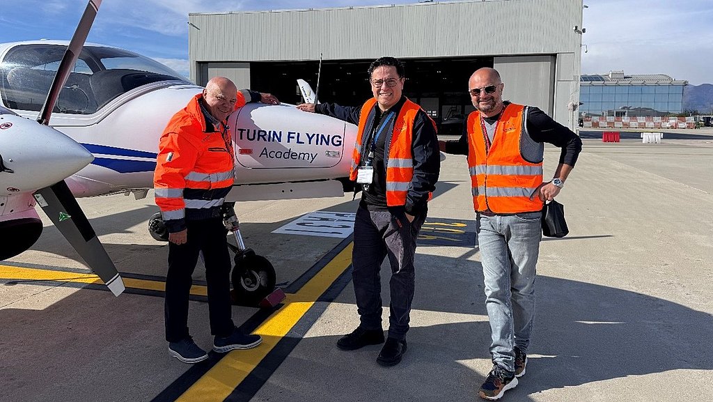 With a hangar in the background, three men in safety vests stand proudly by a DA42-VI training aircraft.