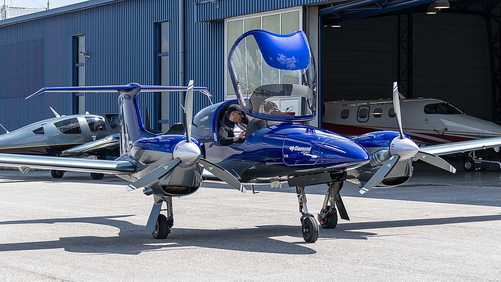 Bue DA42-VI stanind in front of a hanger with two men sitting in the cockpit. 